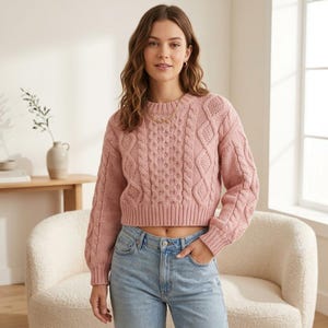 Può includere: Un maglione a maniche lunghe rosa polvere con un motivo a trecce grosse, scollo rotondo e orlo corto. Il capo è abbinato a un paio di jeans in denim azzurro con una classica chiusura a bottone e cerniera lampo.