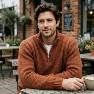May include: A rust-coloured, long-sleeved, quarter-zip jumper with a ribbed collar, cuffs, and hem. The jumper features a silver-toned metal zip pull and is worn over a plain white crew-neck t-shirt, showcasing a chunky knit texture.