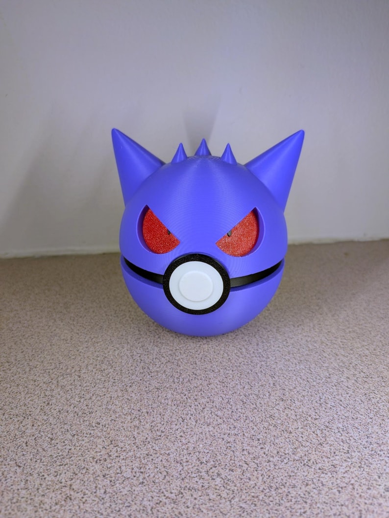 Pode incluir: Uma esfera roxa impressa em 3D com uma faixa preta e um c&iacute;rculo branco, assemelhando-se a uma Pok&eacute; Ball. O topo apresenta orelhas pontudas e espinhos, com cavidades oculares vermelhas texturizadas. Um colecion&aacute;vel &uacute;nico e estilizado.