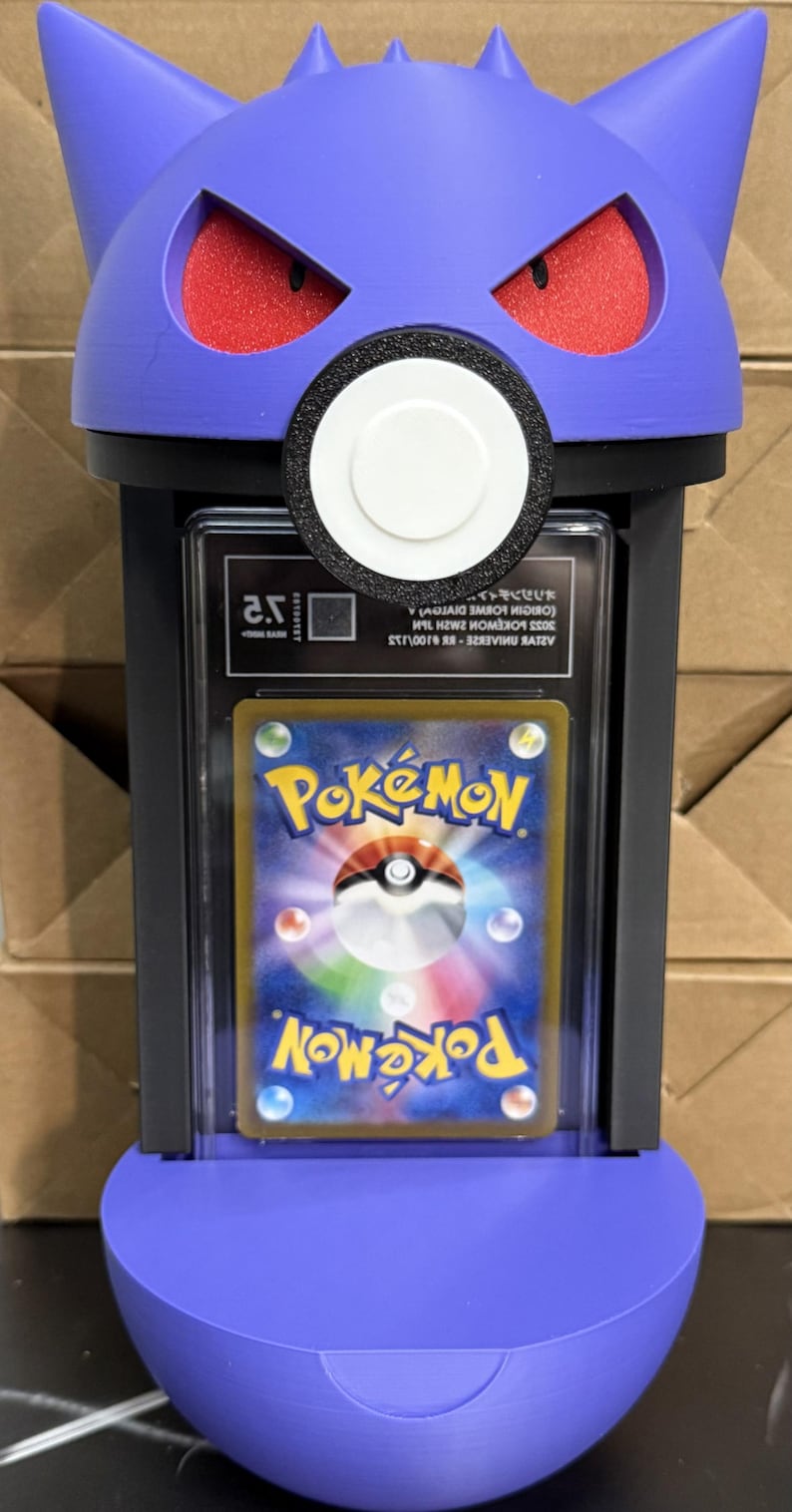 Pode incluir: Um suporte de cart&atilde;o com tema Gengar roxo com olhos vermelhos e um detalhe circular branco. O suporte cont&eacute;m um cart&atilde;o Pok&eacute;mon. O cart&atilde;o apresenta o logotipo Pok&eacute;mon e um design colorido. O suporte foi projetado para exibir o cart&atilde;o.