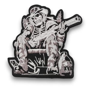 Op de afbeelding: Geborduurde patch met een skelet met een cowboyhoed, zittend en een pistool vasthoudend. Het ontwerp is gedetailleerd met witte en grijze steken op een zwarte achtergrond. De patch heeft een zwarte rand.