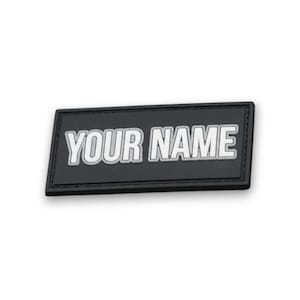 May include: A black rectangular patch with the text "YOUR NAME" in white, outlined in gray. The patch has a stitched border and is likely made of a durable material.