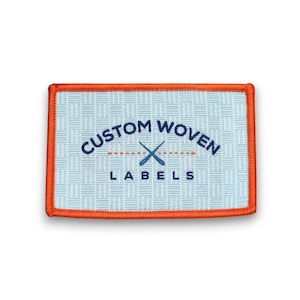 Pode incluir: Etiqueta retangular tecida com borda laranja. A etiqueta tem um fundo azul claro com um padrão tecido. O texto "CUSTOM WOVEN LABELS" é azul escuro, com remos cruzados no centro.