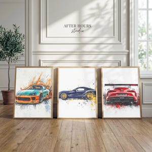 May include: Three framed art prints featuring watercolor paintings of sports cars. The cars are in teal and orange, navy blue, and red. The artwork has a splatter paint effect with gold frames. The text "AFTER HOURS studio" is at the top.