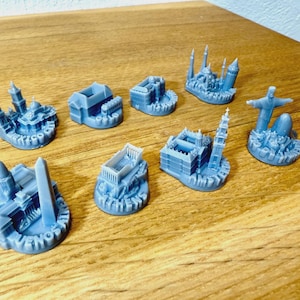 May include: A selection of light blue miniature architectural models, including a church, a building with a tall spire, and a statue of Christ the Redeemer. The models are arranged on a wooden surface.