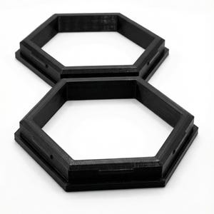 May include: Two black, hexagonal frames are stacked on a white background. The frames have a stepped design and small holes. The frames appear to be 3D-printed. The frames are likely for crafts or home decor.