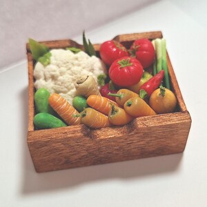 Può includere: Una cassa di legno piena di verdure in miniatura. La cassa contiene cavolfiore, pomodori, carote, peperoni e altri prodotti. Le verdure sono dai colori vivaci e disposte in una cassa di legno rustica.