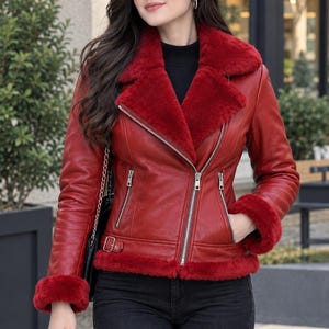 May include: A red leather jacket featuring a wide faux fur collar, matching red faux fur trim on the cuffs and hem, silver-toned metal zippers on the front and side pockets, and a small adjustable side buckle strap at the waist.