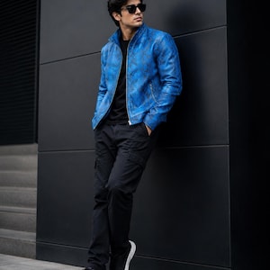 May include: A vibrant blue jacket featuring a detailed snakeskin pattern, a high collar, and a silver front zipper. The jacket is worn over a plain black t-shirt, paired with black cargo trousers and black sneakers with white soles.