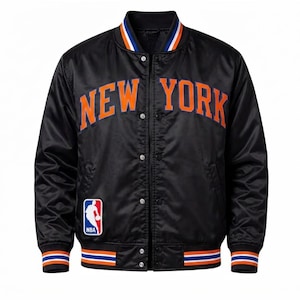 May include: A black satin varsity jacket featuring the text NEW YORK in orange lettering across the chest. The jacket has a snap-button front closure, a ribbed collar and cuffs with orange and white stripes, and an NBA logo patch on the lower right.