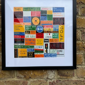 May include: A framed art print featuring a grid of colourful, hand-painted signs and text blocks mimicking urban signage. The composition includes phrases like TAXI, BREAKFAST CLUB, XXX RATED, GOLF, and various other city-inspired labels in a variety of bright colours.