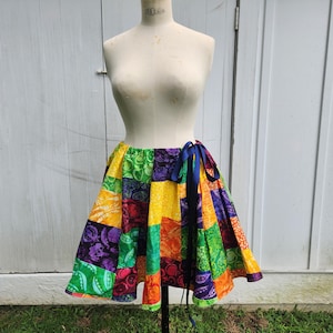 Puede incluir: Una falda de retazos colorida con un lazo azul para atar. La falda está hecha de diferentes telas con una variedad de patrones, incluyendo diseños florales, geométricos y abstractos. La falda es una mezcla vibrante de amarillo, verde, naranja, morado y rojo.