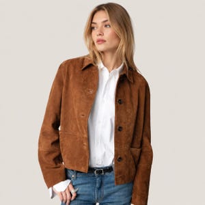 May include: A brown suede jacket with a button-up front, collar, and two front pockets. The jacket is worn over a white button-down shirt and blue jeans. The jacket has a classic, timeless design.