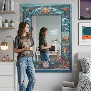 May include: A large rectangular mirror with a blue and teal ocean-themed border. The border features waves, seashells, and fish. The mirror reflects a person wearing a gray t-shirt and blue jeans. The mirror has a neon sign that says "dream always".