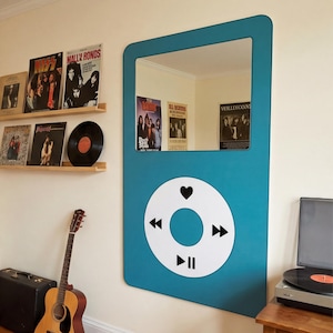 May include: A teal-colored wall mirror shaped like a music player, with a white circular control panel featuring a heart, play/pause, and forward/backward buttons. The mirror reflects posters and records.