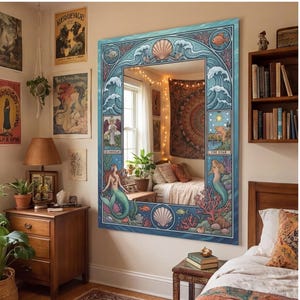 May include: Large rectangular mirror with a blue frame featuring a mermaid and ocean-themed design. The frame includes illustrations of waves, seashells, and fish. The mirror is hanging on a wall in a bedroom with bohemian decor.