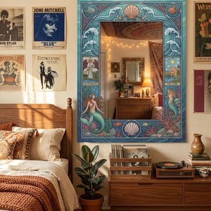 May include: A large, rectangular mirror with a blue, ocean-themed frame featuring mermaids, seashells, and waves. The mirror hangs above a wooden dresser, reflecting the room. Album covers and a record player are visible.