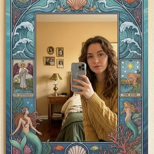May include: Decorative wall mirror with a blue border featuring mermaids, seashells, and ocean waves. The mirror's design includes tarot card illustrations of "The Temperance" and "The Star". The mirror reflects a person taking a selfie.