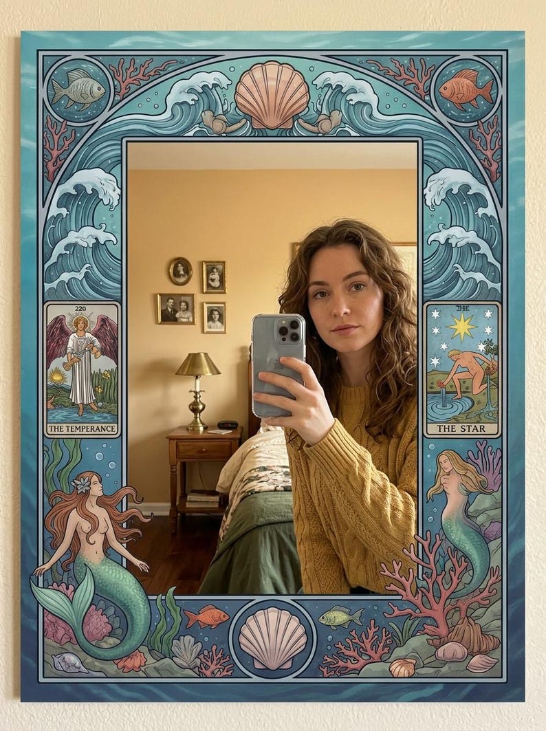 May include: Decorative wall mirror with a blue border featuring mermaids, seashells, and ocean waves. The mirror's design includes tarot card illustrations of "The Temperance" and "The Star". The mirror reflects a person taking a selfie.