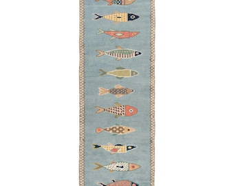Peut inclure: Un tapis de couloir rectangulaire au fond bleu clair orné d'une colonne verticale de onze poissons stylisés aux couleurs et motifs géométriques variés. Le tapis est bordé d'une frise à carreaux marron et blancs et présente des franges blanches.