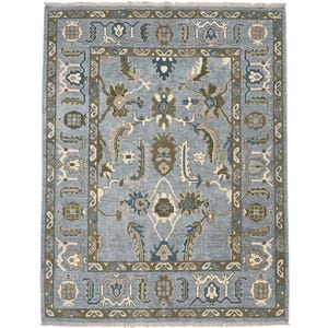 Pode incluir: Um tapete retangular com fundo azul claro e um padrão simétrico de motivos florais e botânicos em verde-azeitona, azul-escuro e creme. O tapete tem uma borda decorativa larga e franjas curtas nas extremidades superior e inferior.
