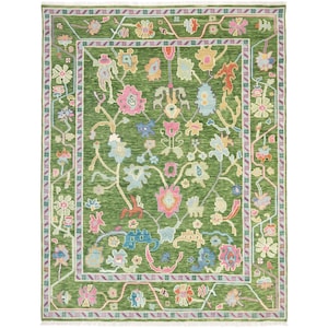 May include: A rectangular area rug featuring a deep green background with a central floral pattern in shades of pink, light blue, yellow, and white. The rug is framed by a decorative border with repeating flower motifs and has white fringe at both ends.