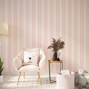 May include: A light pink armchair with wooden legs and a white pillow featuring a bear face. The background is a pink striped wallpaper. A small side table with vases and a basket are also visible.