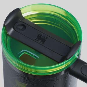 May include: Close-up of a black and green travel mug. The lid is black with a green rim and a bear logo. The mug's body is black with a textured pattern. The handle is black.