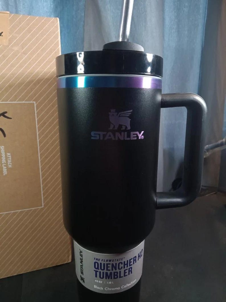 Op de afbeelding: Een zwarte Stanley Quencher H2.0 Flowstate tumbler met een handvat en een rietje. De tumbler heeft een zwart deksel met een kleurrijke iriserende band. De tumbler is 1,18L.