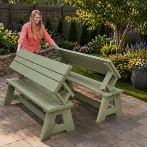 May include: Two light green wooden benches with folding backs are displayed outdoors on a brick patio. The benches are made of wood and have a simple, functional design. The background features a garden with flowers and trees.