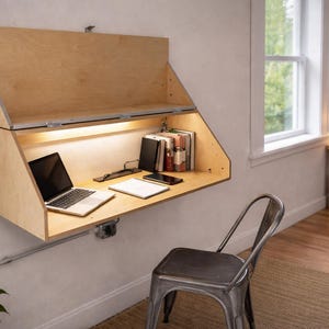 May include: A wall-mounted wooden desk with a laptop, books, and a notebook. The desk has a built-in light and a hinged top. A metal chair sits in front of the desk. The desk is 36 inches wide.