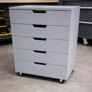 May include: A gray, five-drawer cabinet on wheels. Each drawer has a recessed handle. The cabinet is a solid, rectangular shape, suitable for storage. The cabinet is in a workshop setting.