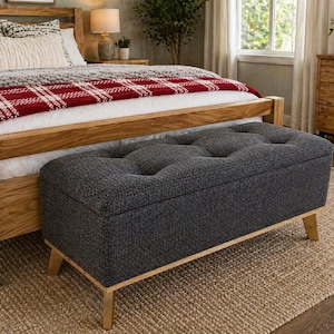 May include: A dark gray upholstered storage bench with button tufting, set at the foot of a wooden bed. The bed has a red and white plaid blanket and decorative pillows. The bench is 48 inches long.