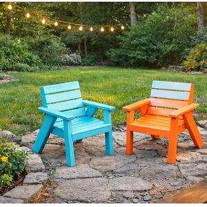May include: Two brightly colored wooden Adirondack chairs. One is painted a vibrant blue, the other a cheerful orange. Both have armrests and slatted backs. They are set on a stone patio in a backyard setting.
