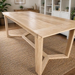 May include: A light-colored wooden dining table with a rectangular top and angled legs. The table is set on a woven jute rug. The table's design is modern and minimalist, suitable for a dining room.
