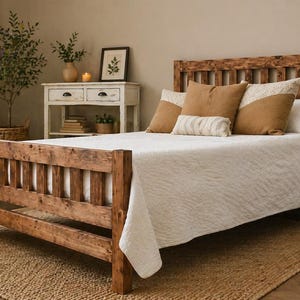 May include: A rustic wooden bed frame with a headboard and footboard. The bed is covered with a white quilt and adorned with brown and cream-colored pillows. The room features a neutral color palette with a woven rug.