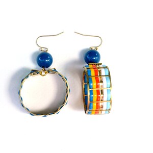 May include: A pair of gold hoop earrings with blue and white enamel. One earring has a blue bead at the top and the other has a colorful striped design.
