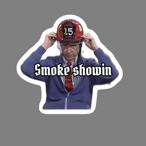 May include: A sticker featuring a person wearing a red firefighter helmet with the number 15 on it, a blue zip-up sweater, and a red tie. The text "Smoke showin" is written in a stylized font.