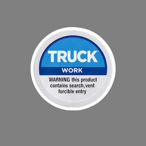 May include: A circular sticker with a white border and a blue center. The word "TRUCK" is in bold white letters above "WORK". Below, the text reads: "WARNING this product contains search, vent forcible entry."