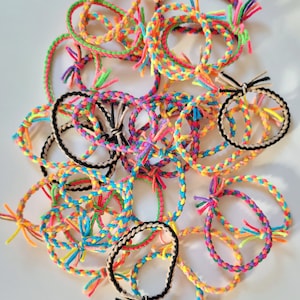 May include: A pile of colorful braided hair ties with tassels. The hair ties are made of a variety of colors, including pink, blue, green, yellow, and black.