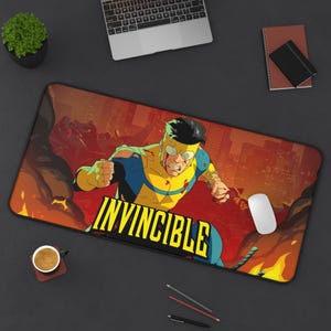 May include: A rectangular mouse mat featuring the character Invincible from the comic book series. The design shows Invincible in action against a fiery cityscape background, with the word "INVINCIBLE" in bold yellow letters.