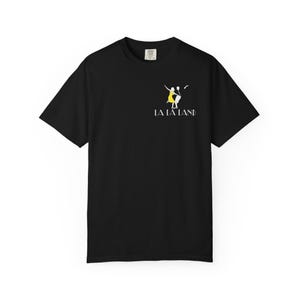 May include: Black t-shirt featuring a graphic from the movie "La La Land." The design includes a yellow dress and a dancing couple. The words "LA LA LAND" are printed in white below the graphic. The shirt has short sleeves and a crew neck.