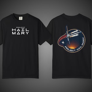 Könnte beinhalten: Ein schwarzes Kurzarm-T-Shirt mit dem weißen Schriftzug "PROJECT HAIL MARY" auf der Brust. Die Rückseite zeigt eine kreisförmige Grafik eines Raumschiffs, das eine Sonne umkreist, mit dem Text "PROJECT HAIL MARY" am unteren Rand.