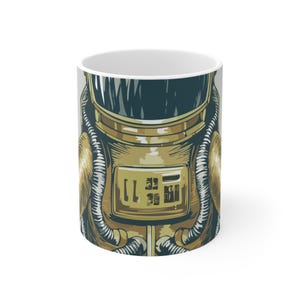 May include: White ceramic mug featuring a detailed illustration of an astronaut's helmet and suit in shades of gold, teal, and gray. The design includes intricate details of the helmet and suit, with the number "11" visible on the front.