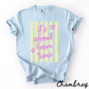 May include: Pale blue t-shirt featuring yellow vertical stripes and the pink text "It's about bam time". Two pink stars are on either side of the text. The word "Chambray" is written in black script at the bottom.