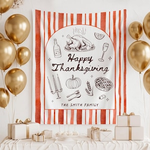 Op de afbeelding: Een rechthoekige stoffen wandhanger met een witte achtergrond en verticale oranje strepen. Het midden toont een bruine lijntekening van een gebraden kalkoen, wijn, een pompoen, een taart en de tekst Happy Thanksgiving THE SMITH FAMILY.