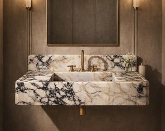 May include: A luxurious bathroom sink made of white marble with black veining. The sink has a gold faucet and is mounted on a wall. A mirror hangs above the sink, and two sconces flank the mirror. A small vase of flowers sits on the counter.