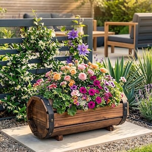 Peut inclure: Un bac en bois en forme de tonneau rempli de fleurs colorées, dont des roses et des pétunias. Le bac marron est orné de bandes métalliques noires et repose sur une surface en pierre. Le fond est composé de feuillage vert et d'une clôture grise avec des plantes grimpantes.