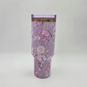 Puede incluir: Un vaso de color lavanda con un dise&ntilde;o floral. El vaso presenta una banda dorada cerca de la parte superior y una tapa transparente. El patr&oacute;n floral incluye flores rosas, moradas y blancas. El vaso est&aacute; dise&ntilde;ado para contener unos 887 ml.