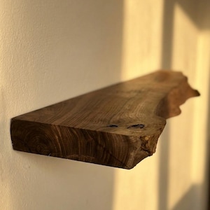 May include: A floating wooden shelf with a natural edge, mounted on a light-colored wall. The shelf is a rich brown color, showcasing the wood grain. The shelf is approximately 30 inches long.